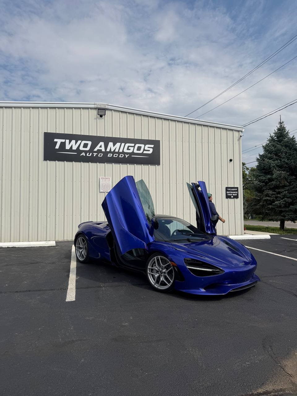 Blue McLaren 750S side view with doors raised outside the Two Amigos Auto Body shop