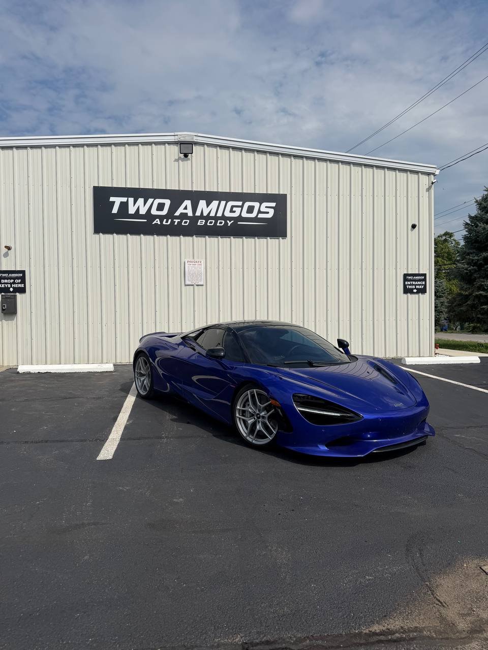 Blue McLaren 750S front three-quarter view outside the Two Amigos Auto Body shop