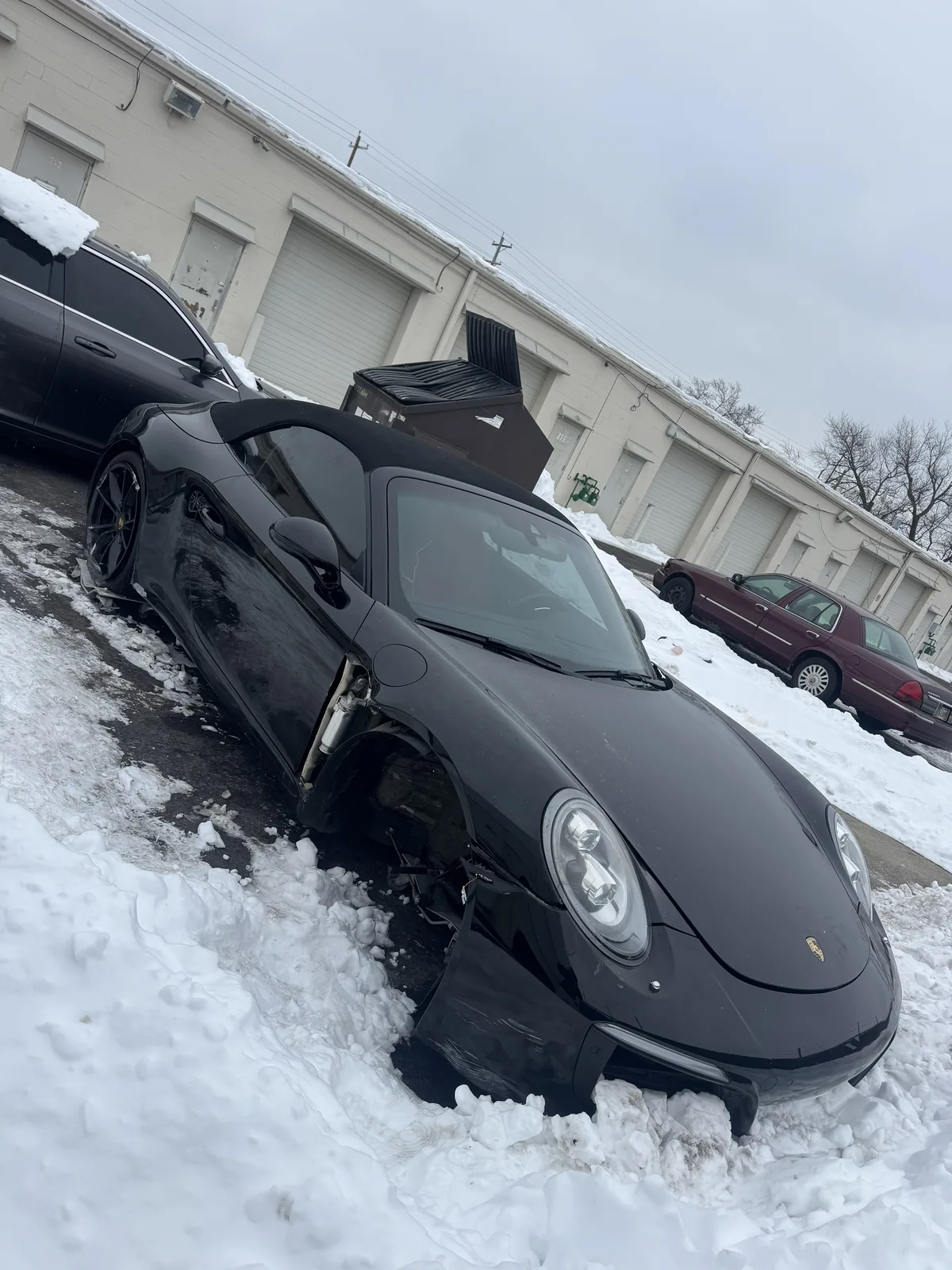 Black Porsche 911 cabriolet with front wheel and fender damage in snow
